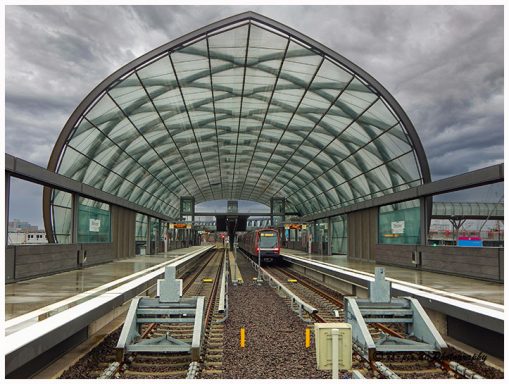 Moderne U-Bahn-Station mit gewölbtem Glasdach und leeren Gleisen.