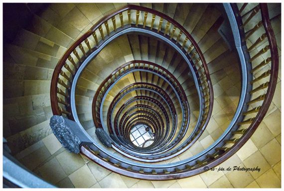 Eine spiralförmige Treppe mit Holzgeländer und zentralem Lichtfenster.