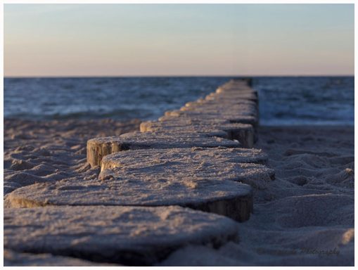 Holzsteg führt über den Sand zum Meer bei Sonnenuntergang.