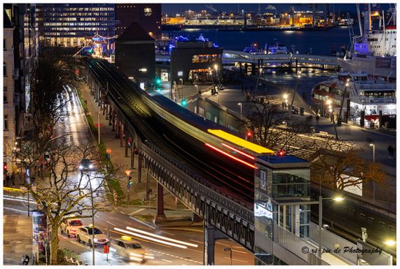 Beleuchtete Stadtansicht mit einer vorbeifahrenden Bahn und nächtlicher Umgebung.