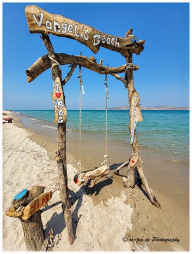 Schaukel aus Holz am Strand mit Meer und blauen Himmel im Hintergrund.