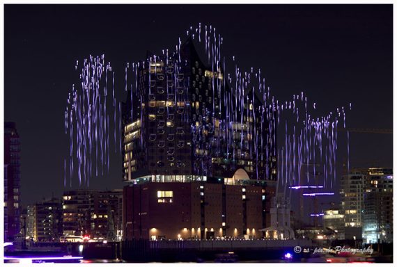 Lichtshow mit Wasserfällen aus Farben über einem modernen Wolkenkratzer bei Nacht.
